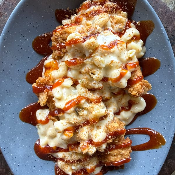 Fried chicken and macaroni and cheese drizzled with hot sauce and barbecue sauce on a blue plate.
