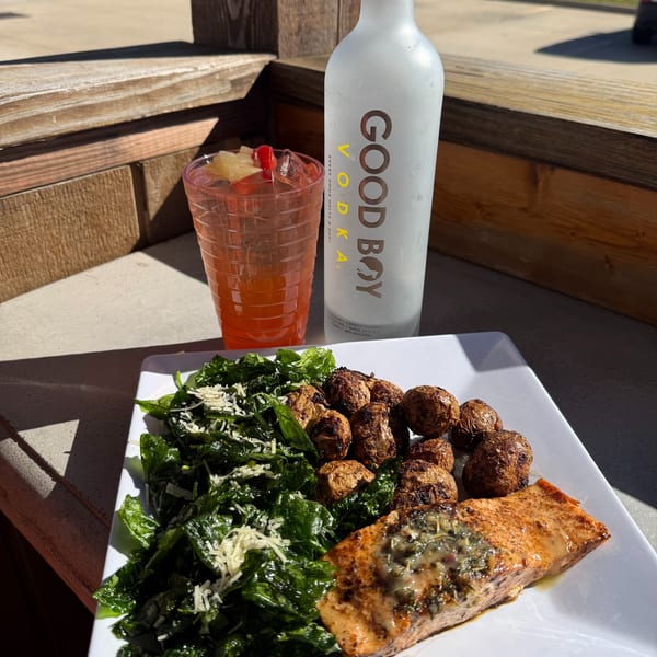 Grilled salmon with roasted potatoes, spinach, and a cocktail next to a bottle of Good Boy Vodka.