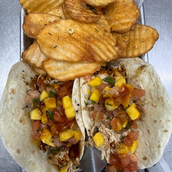 Two chicken tacos with mango salsa and waffle fries on a metal tray with paper liner.