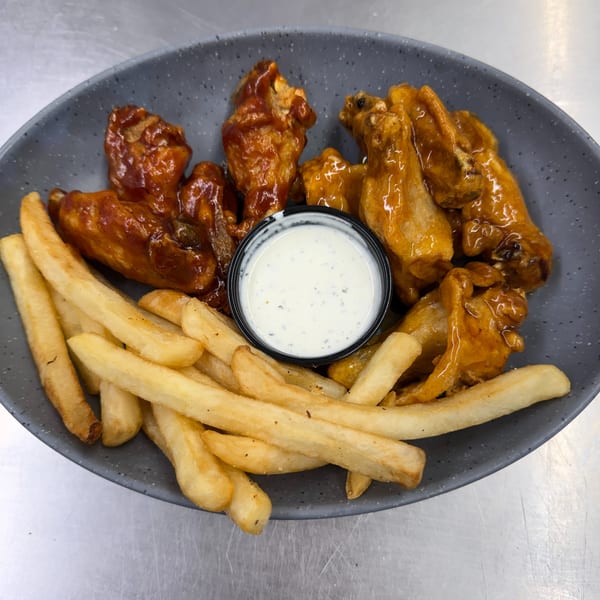 A gray plate holds two kinds of chicken wings, French fries, and a cup of ranch dressing.