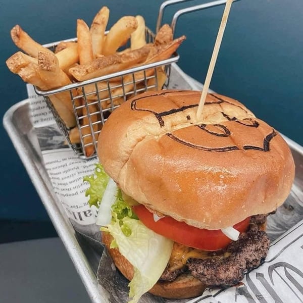 A cheeseburger with lettuce, tomato, and onion, served with a side of french fries.