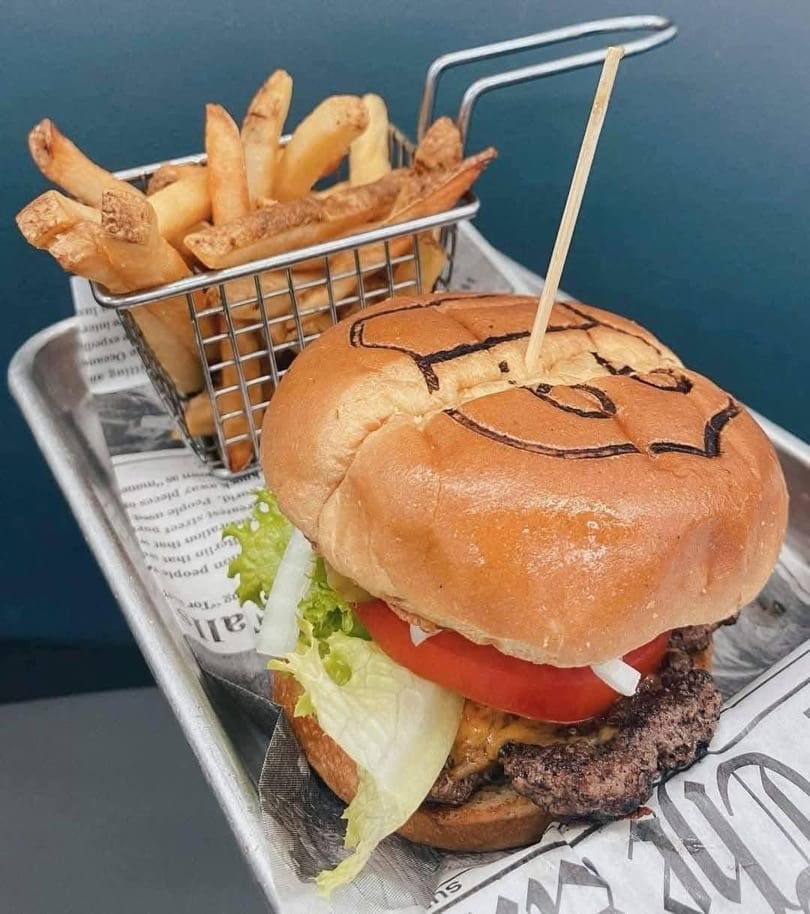 A cheeseburger with lettuce, tomato, and onion, served with a side of french fries.