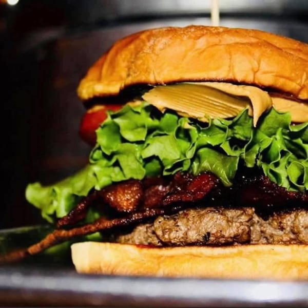 Close-up of a juicy burger with bacon, lettuce, tomato, and a creamy sauce.