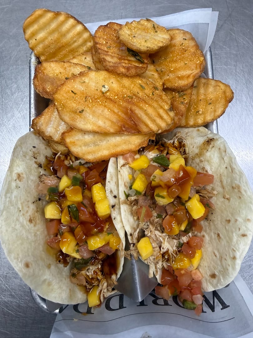 Two chicken tacos with mango salsa and a side of waffle-cut fries on a metal tray.